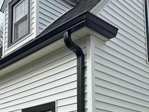 Black gutter and downspout with offset elbows on a house with white siding and a dormer