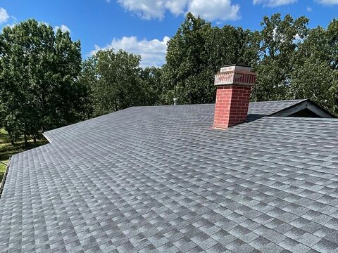 Gray architectural shingle roof with a red chimney, trees and a blue sky with clouds beyond.