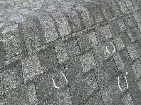 Hail hits circled in chalk on gray asphalt shingles along a roof ridge.