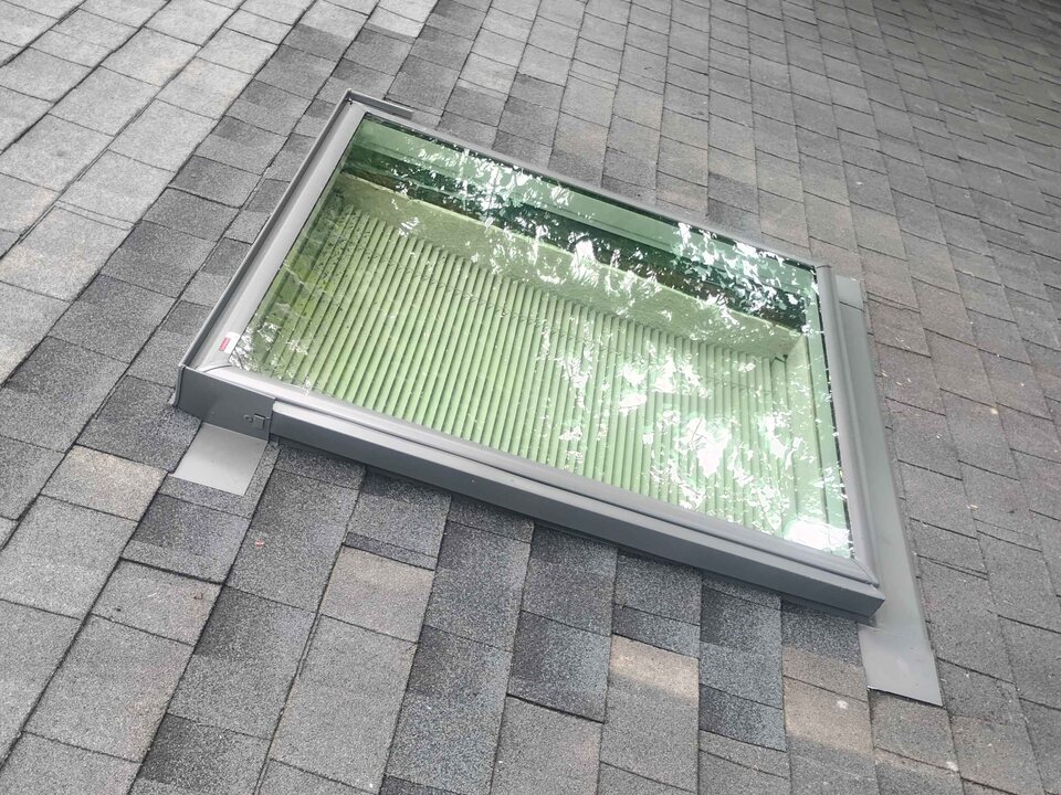 Skylight with gray metal flashing set into a sloped gray shingle roof.