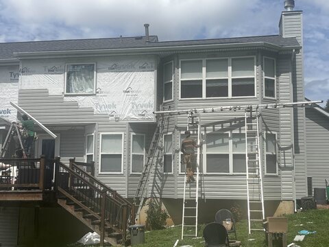 Crew re-siding the rear of a two-story house over house wrap from ladder-jack scaffolding.